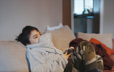 Wall Mural - Kid playing video game in living room,Lifestyle portrait of young boy playing game online holding controller having fun sitting on sofa,Happy Child  holding joystick play alone at home in Winter