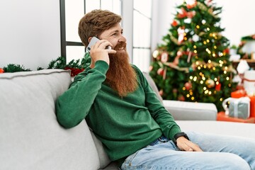 Sticker - Young redhead man talking on the smartphone sitting by christmas tree at home