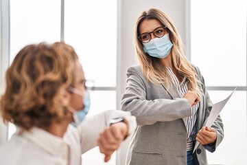 Wall Mural - Man and woman business workers wearing medical mask doing safety greeting at office