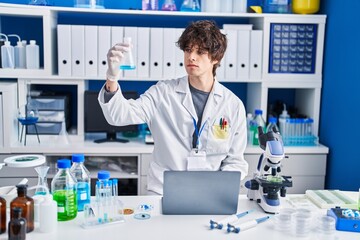 Poster - Young hispanic man scientist using laptop measuring liquid at laboratory