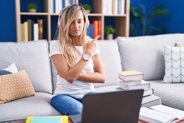 Sticker - Young blonde woman studying using computer laptop at home pointing with hand finger to the side showing advertisement, serious and calm face