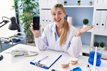 Poster - Beautiful dentist woman showing smartphone screen celebrating achievement with happy smile and winner expression with raised hand