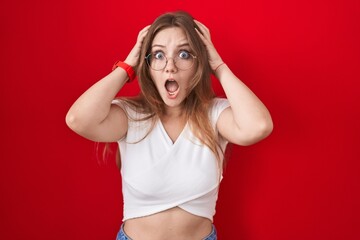 Sticker - Young caucasian woman standing over red background crazy and scared with hands on head, afraid and surprised of shock with open mouth