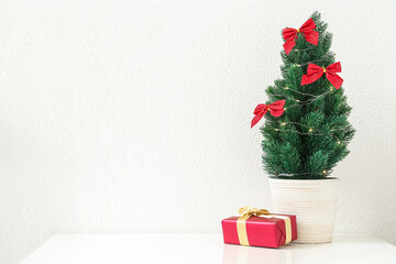 Small Christmas tree with glowing lights and gift on shelf near light wall