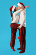 © Pixel-Shot - Young couple in Santa hats hugging on blue background
