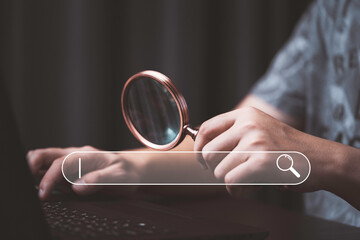 Wall Mural - Man holding magnifier glass and using computer laptop with search bar icon for Search Engine Optimization or SEO concept to find information by internet connection.