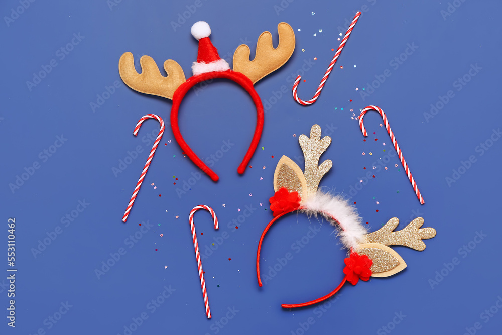 Composition with Christmas reindeer horns headbands and candy canes on blue background