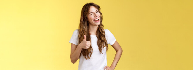 I support you guys good luck. Happy cheerful cheeky attractive girl wink approval like show thumb up smiling broadly satisfied awesome party congratulating friend well done yellow background