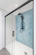 White bathroom with glass shower, walls are decorated with herringbone tiles in pale blue. Black shower system enclosure with dark matte framed sliding glass door. Bright modern and stylish bathroom