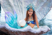 A Beautiful Happy Little Girl In A Mermaid Costume Sits In A Large Sea Shell
