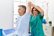 © Krakenimages.com - Middle age man and woman wearing physiotherapy uniform having rehab session stretching arm at physiotherapy clinic