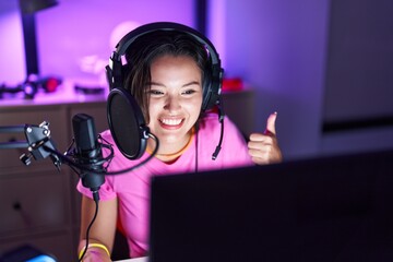 Sticker - Hispanic young woman playing video games smiling happy and positive, thumb up doing excellent and approval sign