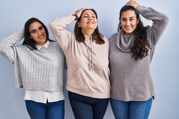 Wall Mural - Mother and two daughters standing over blue background smiling confident touching hair with hand up gesture, posing attractive and fashionable