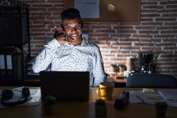 Wall Mural - Young hispanic man working at the office at night smiling doing phone gesture with hand and fingers like talking on the telephone. communicating concepts.