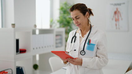 Poster - Middle age hispanic woman wearing doctor uniform using touchpad at clinic