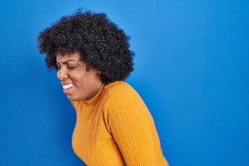 Poster - Black woman with curly hair standing over blue background suffering of backache, touching back with hand, muscular pain