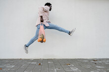 Young Man With Mesh Bag Jumping In Front Of White Wall