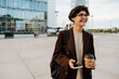 © Drobot Dean - European woman using cellphone and drinking coffee at city street