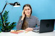 Portrait of confused disappointed troubled secretary employee woman in shirt sit work at white office desk with pc laptop prop up forehead, posing isolated over blue color background wall in studio