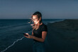 © Westend61 - Woman text messaging through smart phone on beach at night