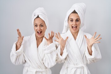 Canvas Print - Middle age woman and daughter wearing white bathrobe and towel celebrating crazy and amazed for success with arms raised and open eyes screaming excited. winner concept