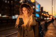 © Westend61 - Smiling woman holding shopping bags using smart phone at dusk