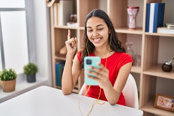 Canvas Print - Young brazilian woman doing video call with smartphone smiling happy pointing with hand and finger to the side