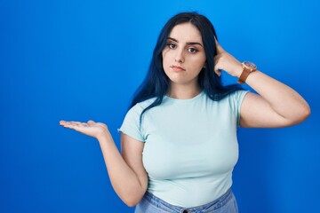 Poster - Young modern girl with blue hair standing over blue background confused and annoyed with open palm showing copy space and pointing finger to forehead. think about it.