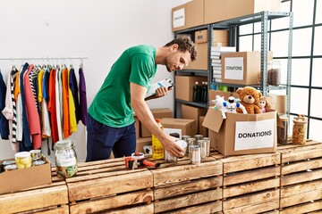 Sticker - Young hispanic man wearing volunteer uniform holding canned food at charity center