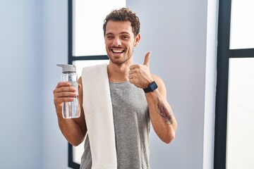 Canvas Print - Young hispanic man wearing sportswear drinking water doing happy thumbs up gesture with hand. approving expression looking at the camera showing success.