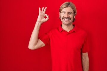 Poster - Caucasian man with mustache standing over red background smiling positive doing ok sign with hand and fingers. successful expression.