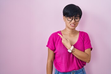 Sticker - Young asian woman with short hair standing over pink background pointing aside worried and nervous with forefinger, concerned and surprised expression