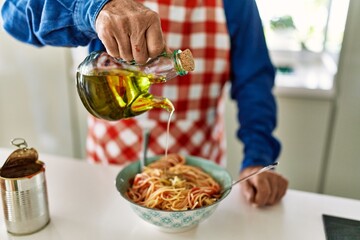 Poster - Senior man pouring oil on spaghetti at kitchen