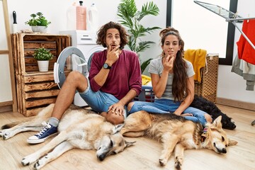 Sticker - Young hispanic couple doing laundry with dogs looking fascinated with disbelief, surprise and amazed expression with hands on chin