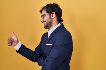 Poster - Handsome latin man standing over yellow background looking proud, smiling doing thumbs up gesture to the side