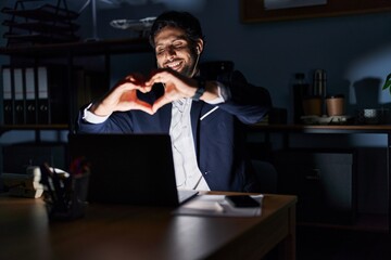 Canvas Print - Handsome latin man working at the office at night smiling in love showing heart symbol and shape with hands. romantic concept.