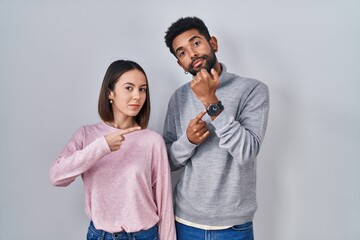 Canvas Print - Young hispanic couple standing together in hurry pointing to watch time, impatience, looking at the camera with relaxed expression