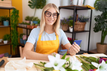 Canvas Print - Young blonde woman florist using smartphone holding credit card at flower shop