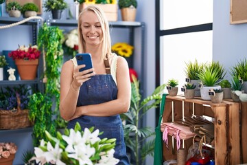 Wall Mural - Young blonde woman florist smiling confident using smartphone at florist store