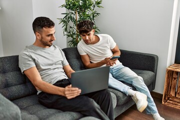 Canvas Print - Two hispanic men couple using smartphone and laptop at home