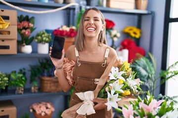 Wall Mural - Young woman working at florist shop showing smartphone screen smiling and laughing hard out loud because funny crazy joke.