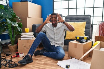 Sticker - African american man sitting on the floor at new home smiling cheerful playing peek a boo with hands showing face. surprised and exited