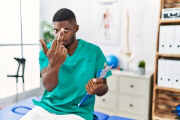 Canvas Print - Young african american man working at pain recovery clinic showing middle finger, impolite and rude fuck off expression