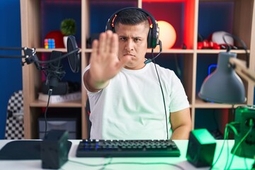 Sticker - Young hispanic man playing video games doing stop sing with palm of the hand. warning expression with negative and serious gesture on the face.