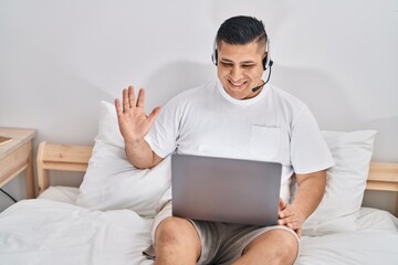 Canvas Print - Hispanic young man using computer laptop on the bed looking positive and happy standing and smiling with a confident smile showing teeth