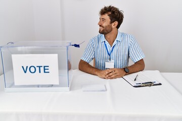 Sticker - Young handsome man at political election sitting by ballot looking to side, relax profile pose with natural face with confident smile.