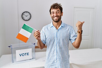 Sticker - Young handsome man at political campaign election holding ireland flag pointing thumb up to the side smiling happy with open mouth