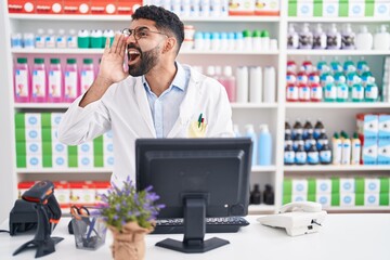 Wall Mural - Hispanic man with beard working at pharmacy drugstore shouting and screaming loud to side with hand on mouth. communication concept.