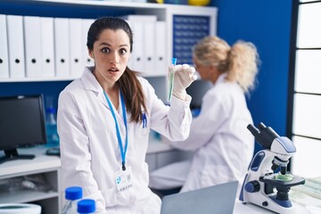 Sticker - Young hispanic woman working at scientist laboratory scared and amazed with open mouth for surprise, disbelief face