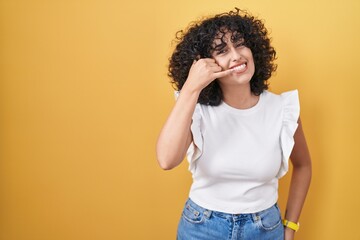 Sticker - Young middle east woman standing over yellow background smiling doing phone gesture with hand and fingers like talking on the telephone. communicating concepts.